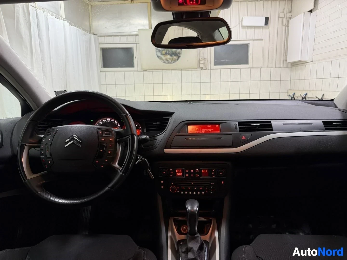 Ohjaamo: Auton kuljettajan paikka sisältä kuvattuna. Näkyvät Citroën-ohjauspyörä ja musta kojelauta, jossa on punainen näyttö.