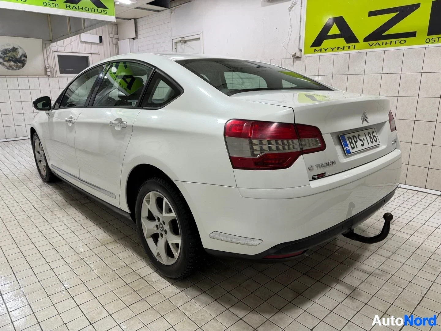 Takaviisto: Valkoinen Citroen C5 sedan näkyy vasemmalta takaa, sisätiloissa. Rekisterikilpi näkyy