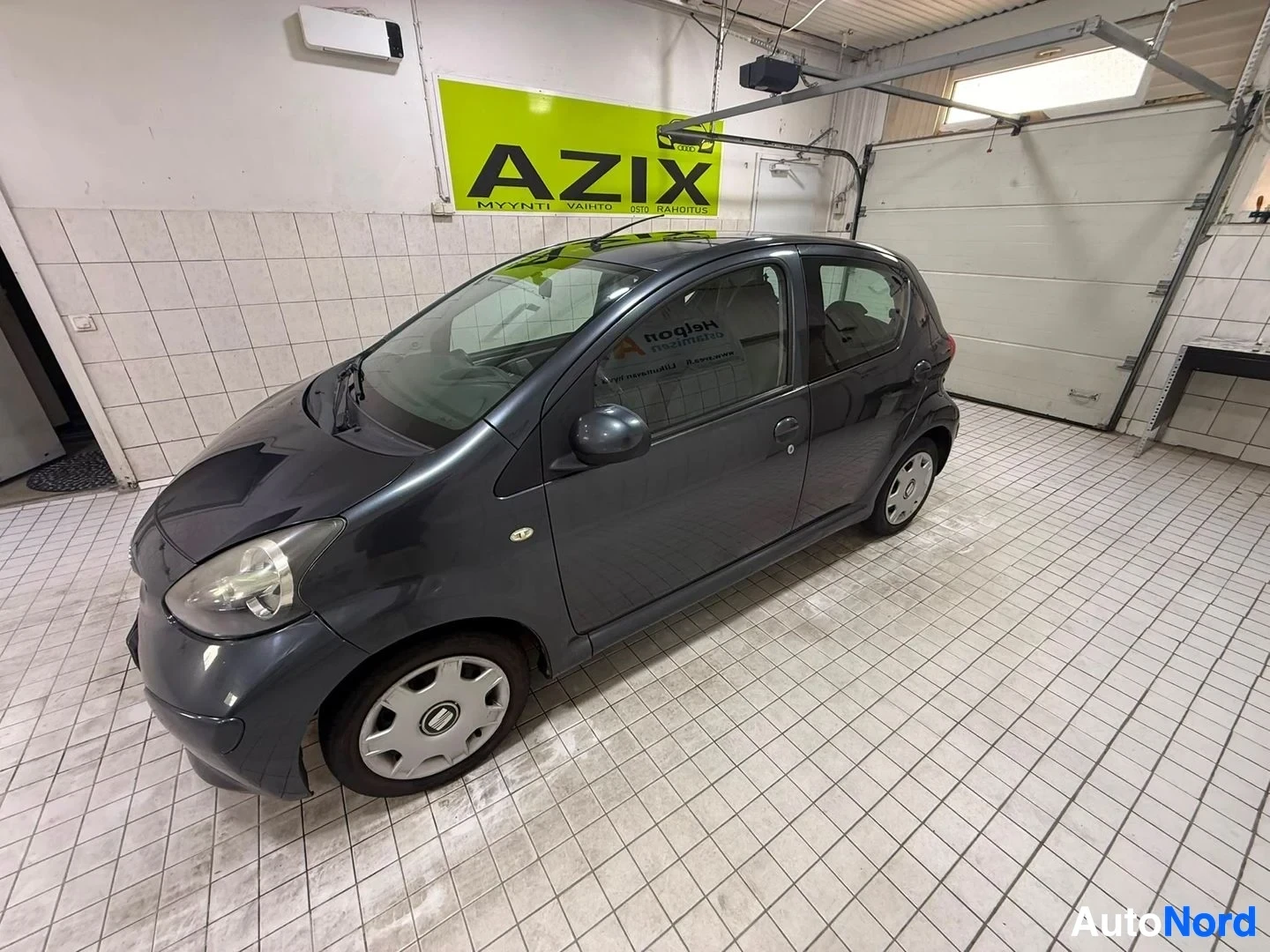 Sivulta: Musta Toyota Aygo kuvattuna sivulta vasemmalta puolelta näyttelyhallissa.
