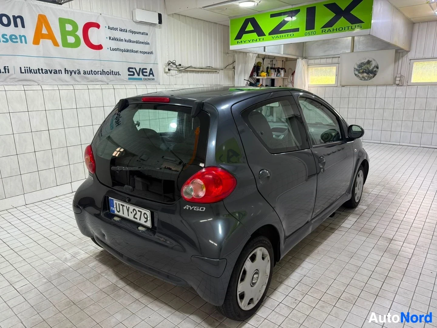 Takaviisto: Musta Toyota Aygo seisoo näyttelyhallissa, kylkea kuvattuna oikealla puolella, rekisterikilpi näkyy