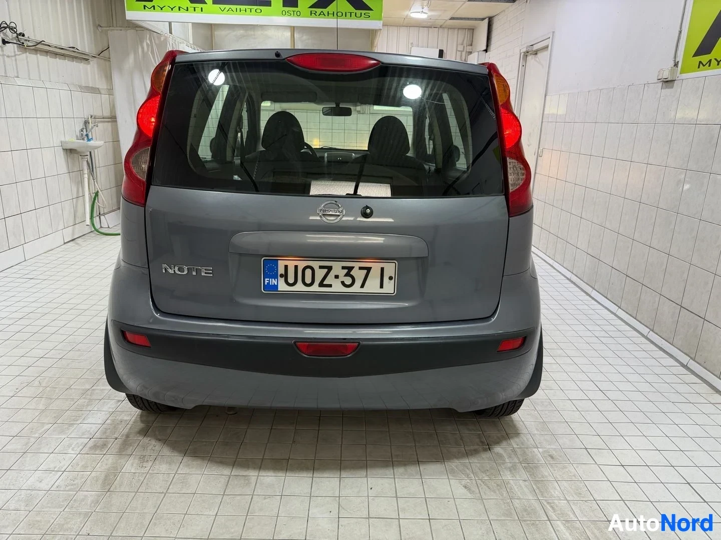 Takaa: Nissan Note -mallinen harmaa viisipaikkainen henkilöauto takaapäin katsottuna sisätiloissa, rekisterikilvessä