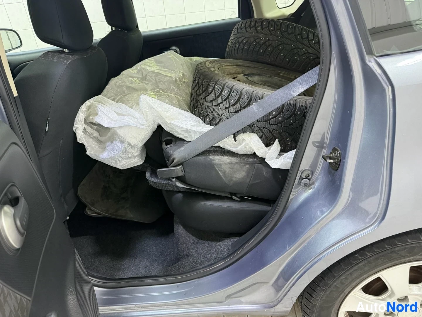 Tavaratila: Auton takakammio, oikealta avattu ovi näkyvissä, talvikellot valkoisissa säkeissä, tumma lattia, musta istuimen selkänoja vasemmalla.