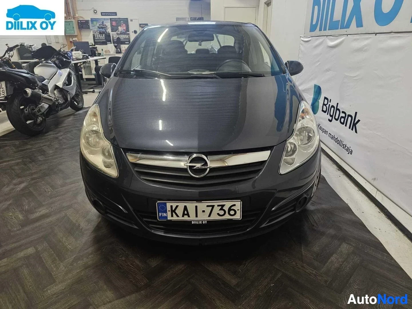 Edestä: Opel Corsa -henkilöauto edestä katsottuna hallissa, tummansininen väri, rekisterikilvessä, Opel-logo grillissä
