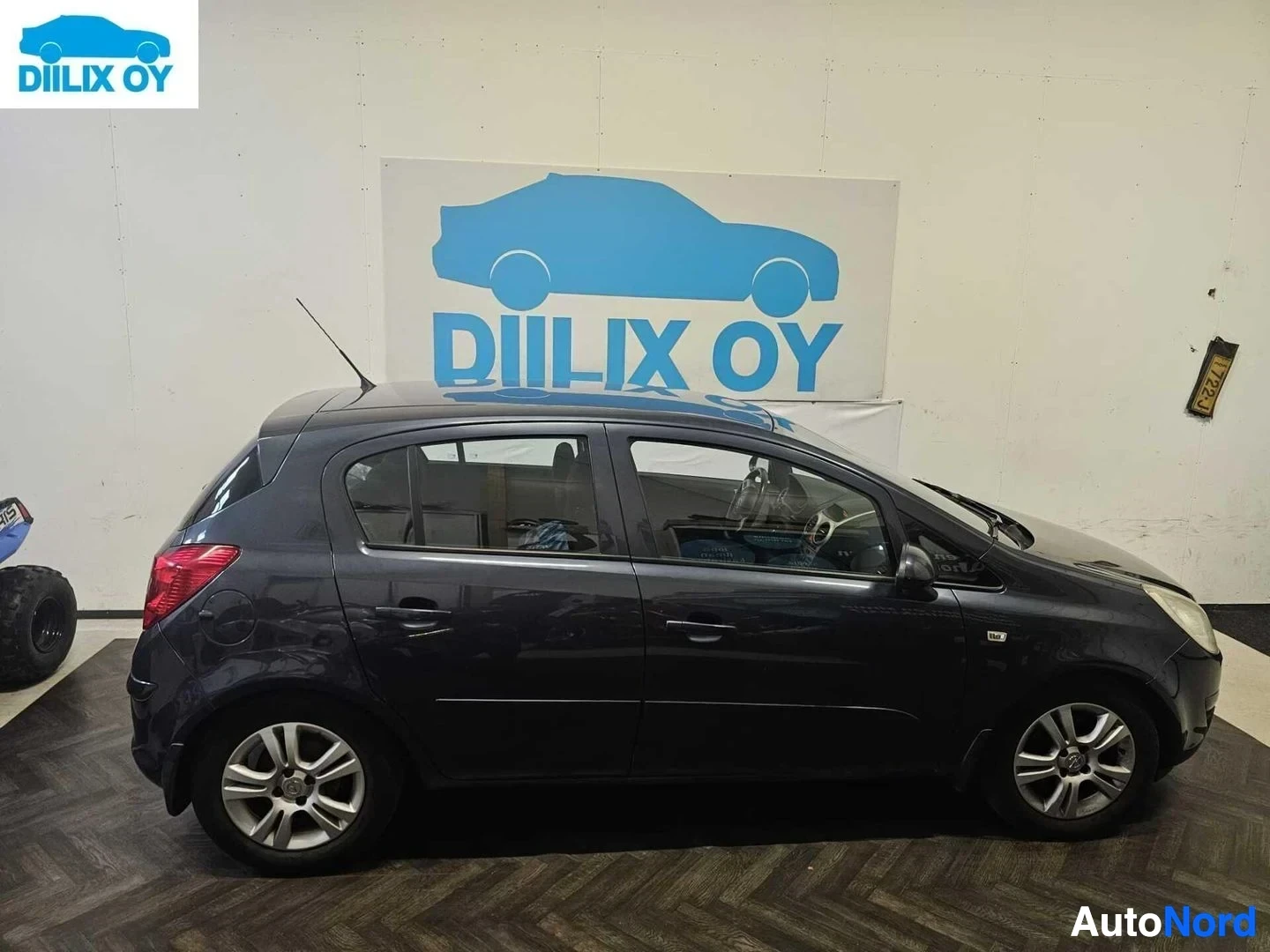 Sivulta: Musta Opel Corsa -henkilöauto sisätiloissa, vasen kylki näkyvissä. Rekisterinumero KA-I-736. Alumiiniset vanteet.