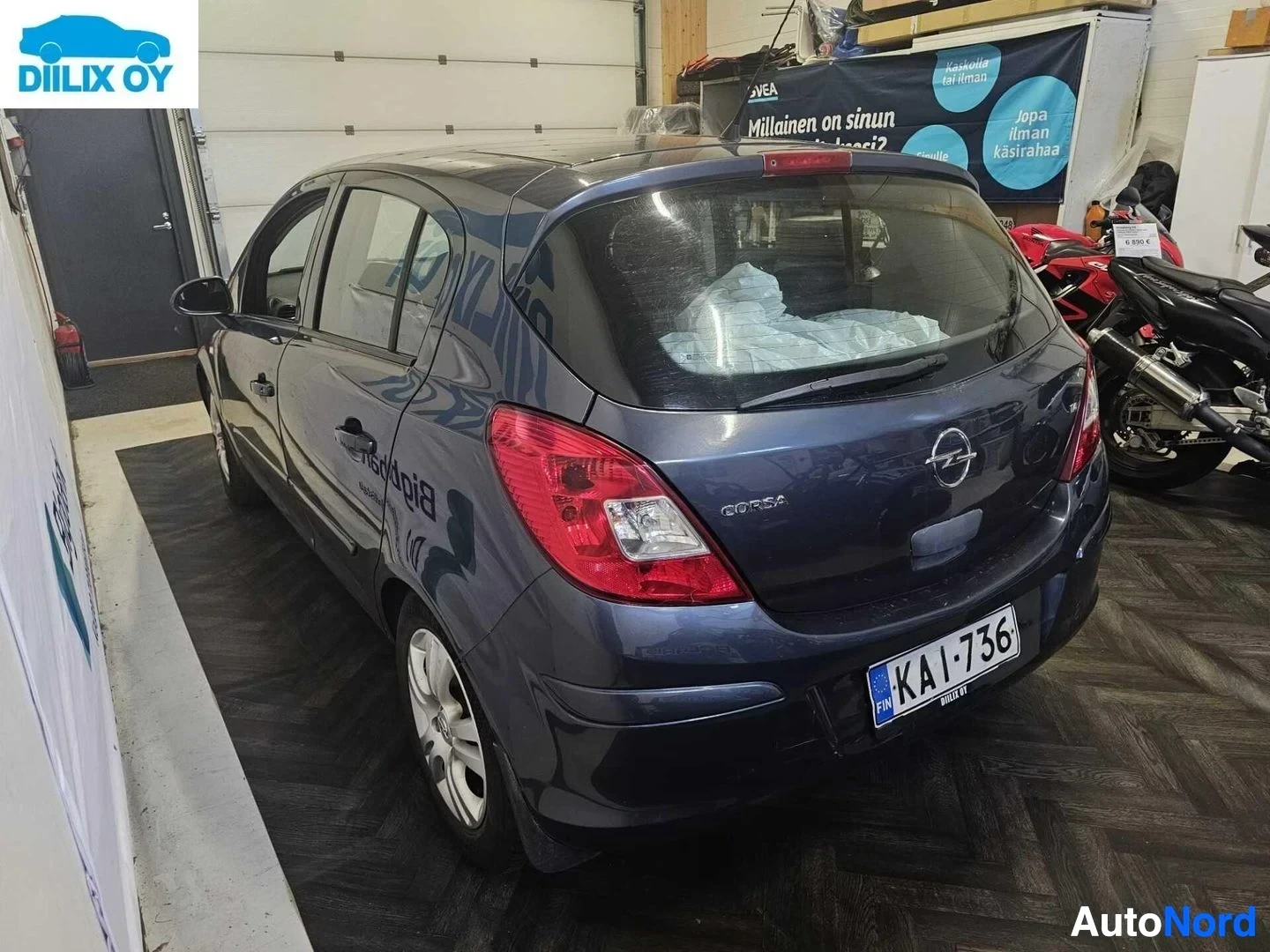 Takaviisto: Musta Opel Corsa -henkilöauto sisätiloissa, takapuoli ja vasemman puoleinen kylki näkyvät. Rekisterinumero KA-I-736. Teksti "Corsa" takaovisssa.