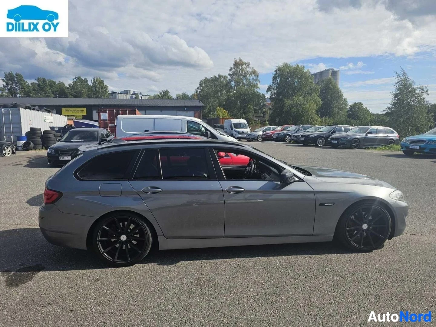 Sivulta: Harmaa BMW-farmari sivunäkymä, ovi auki, punainen istuinverhoilu näkyvissä sisällä.