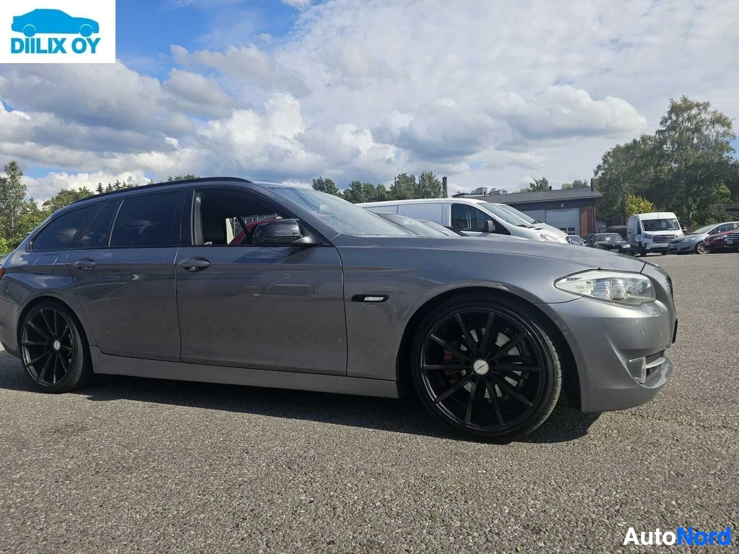 Sivulta: Harmaa BMW-farmari pysäköitynä, näkymä sivulta. Ovi on avoin ja näkyy punainen sisätekstiili. Auto on suunnattu vasemmalle.