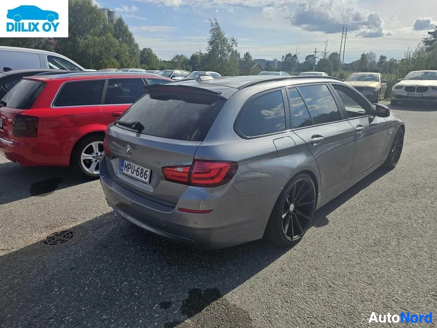 Takaa: Harmaa BMW-farmari takanäkymä, punaisten takavalojen ja rekisterikilven näkyvissä parkkipaikalla.