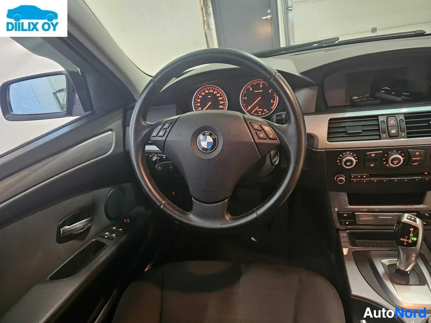 Etuistuimet: Auton kuljettajan puolelta kuvattu mittaritaulu ja ohjauspyörä, näkyvät kaksi pyöreää mittaria punaisella valaistuksella ja BMW-logo ohjauspyörän keskellä.