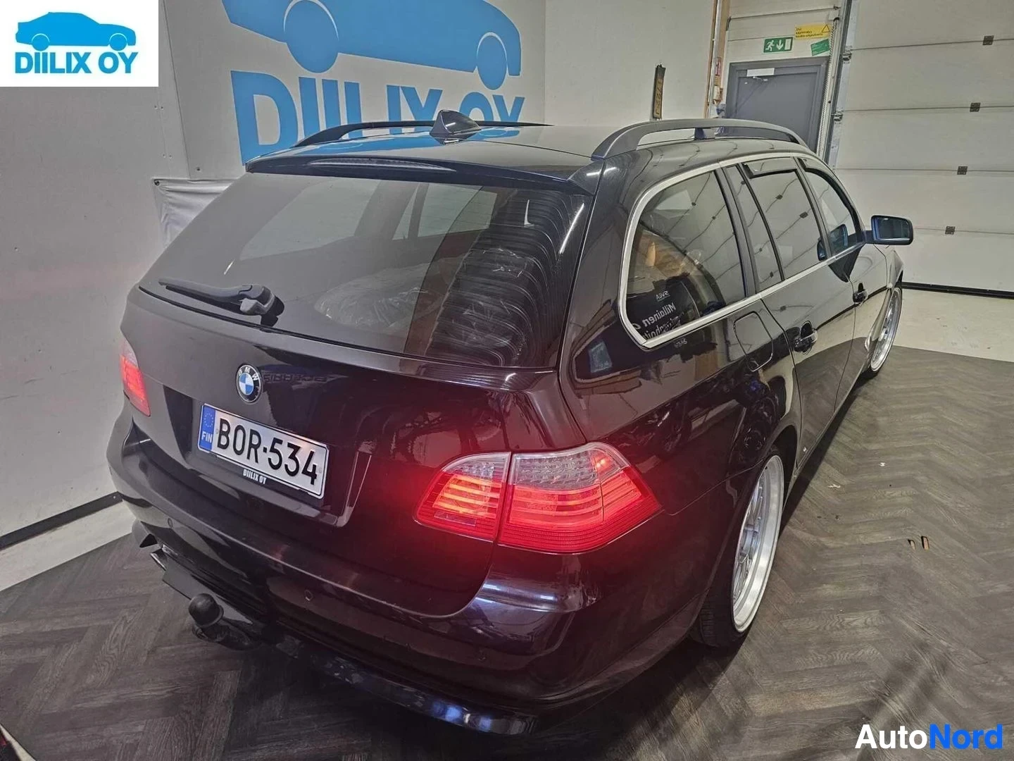Takaviisto: Punainen-musta BMW viistoperä takaosasta oikealle, takavalot punaisia, katto-laturi näkyvissä, rekisterikilpi näkyvissä.