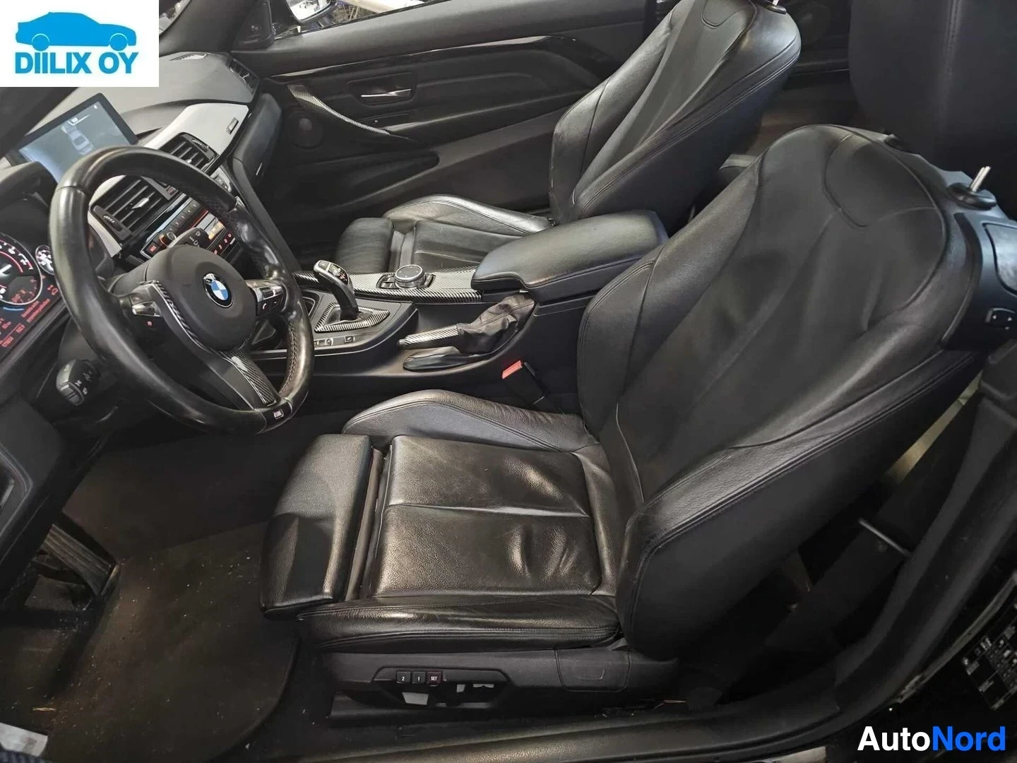 Ohjaamo: BMW auton sisätila, musta nahka istumapaikoilla, kolmisilmukkakehä ohjauspyörässä näkyvissä, automaattivaihtaja välillä