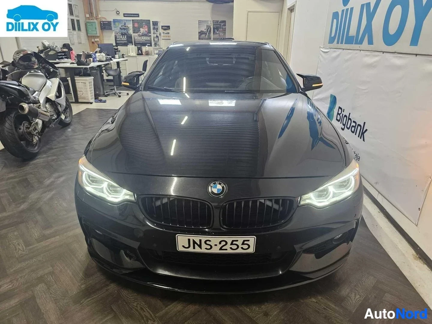 Edestä: Musta BMW sedan sisätiloissa, etupuoli kohti kameraa, rekisterikilvessä teksti, LED-ajovalot näkyvissä