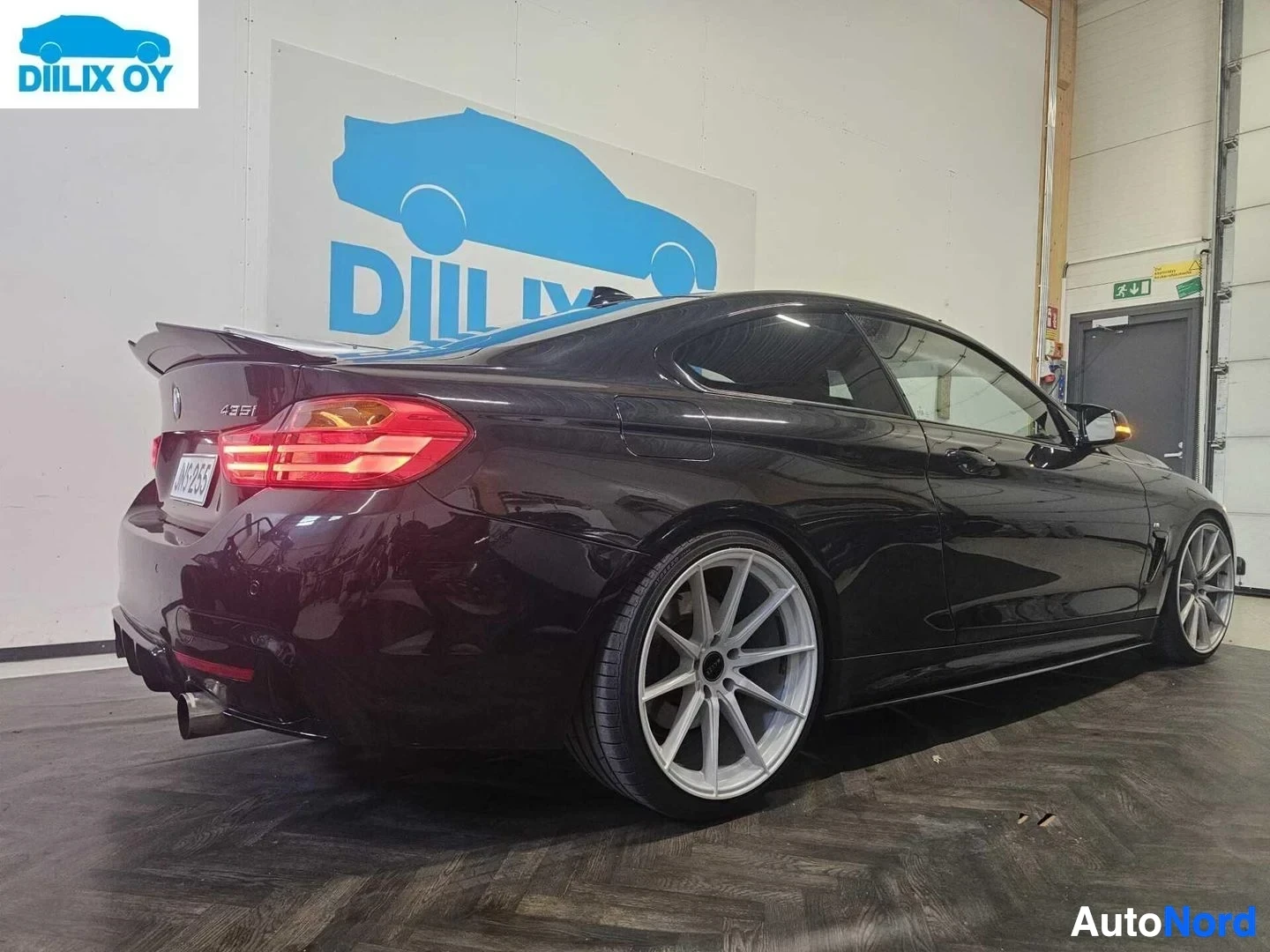 Takaviisto: Viininpunainen BMW-coupe sisätilassa, takaviistosta näkyvä oikea puoli, rekisterikilpi näkyvillä takaa, LED-takavalo näkyvissä.