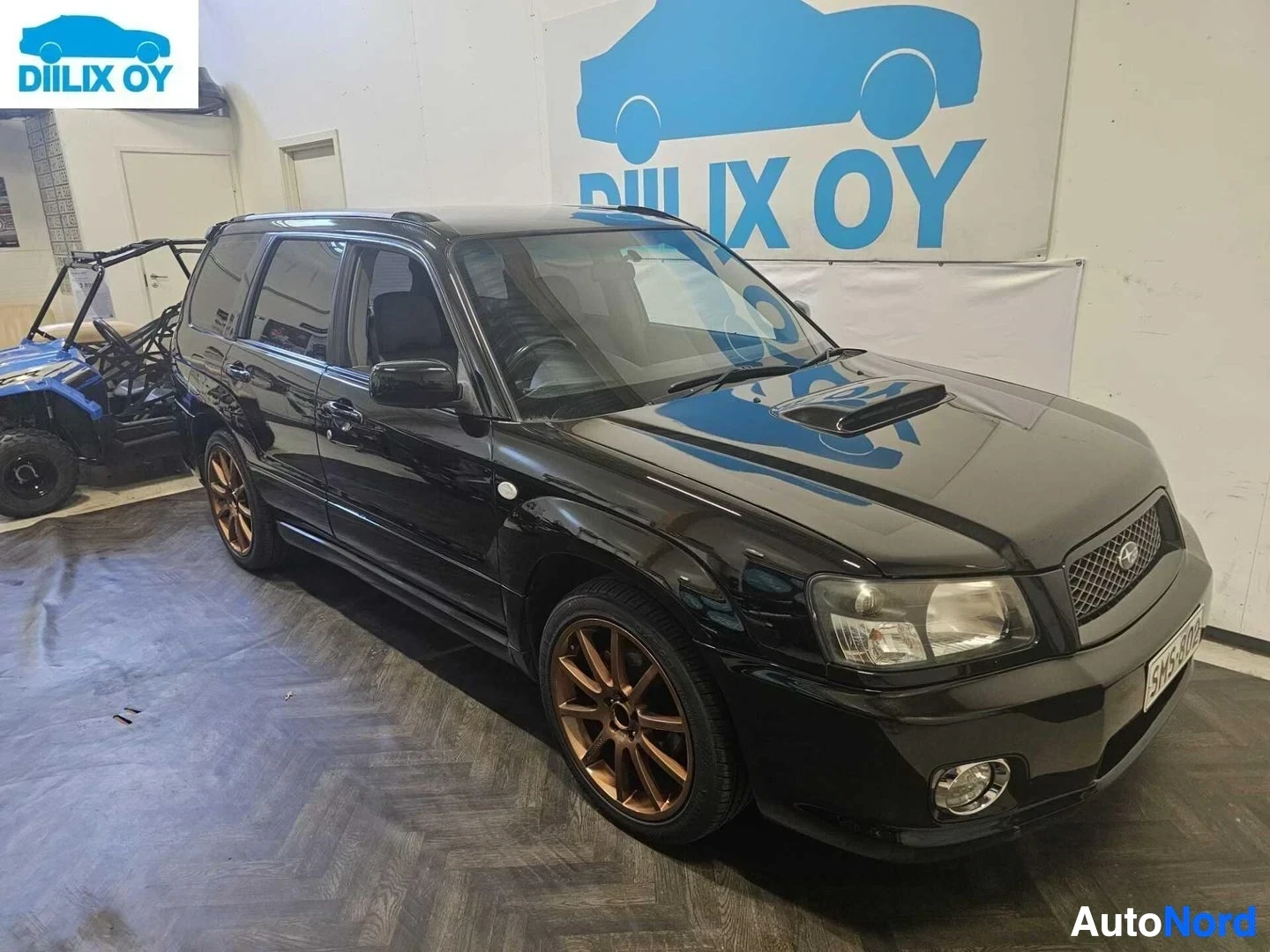 Etuviisto, nokka vasemmalle: Musta Subaru Forester -farmari sisätiloissa, kuvattu kolmen neljänneksen kulmasta vasemmalta. Ajoneuvon etupää osoittaa vasemmalle. Pronssinväriset van
