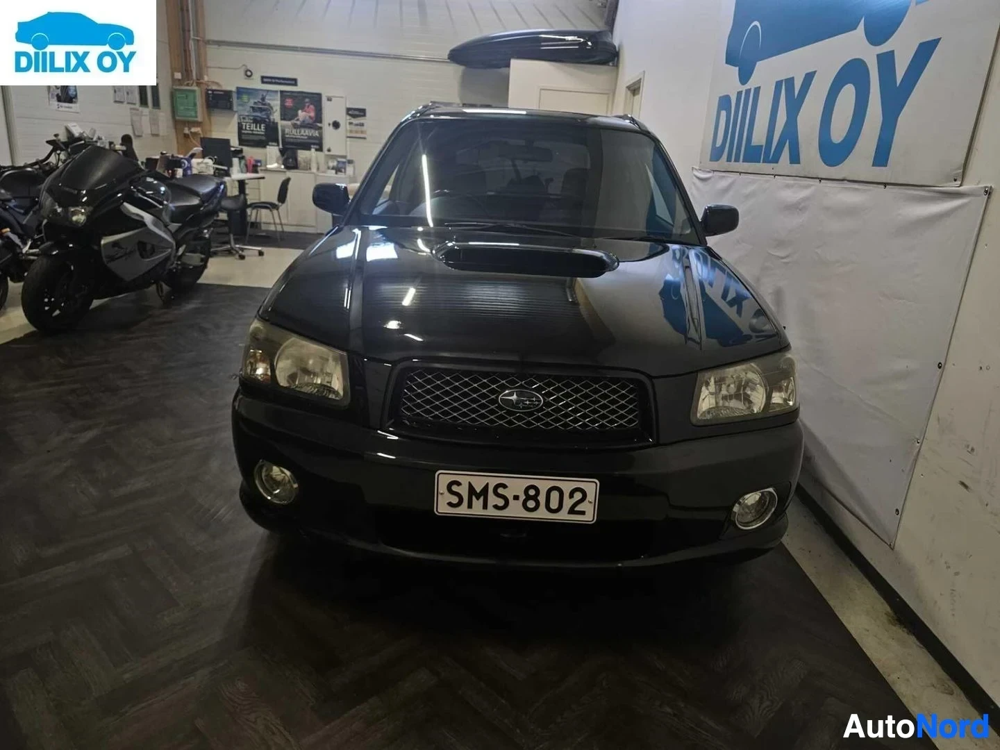 Edestä: Musta Subaru maastoauto edestä, näkyvissä nelikulmainen grilli, pyöreät sumuvalot ja rekisterikilpi
