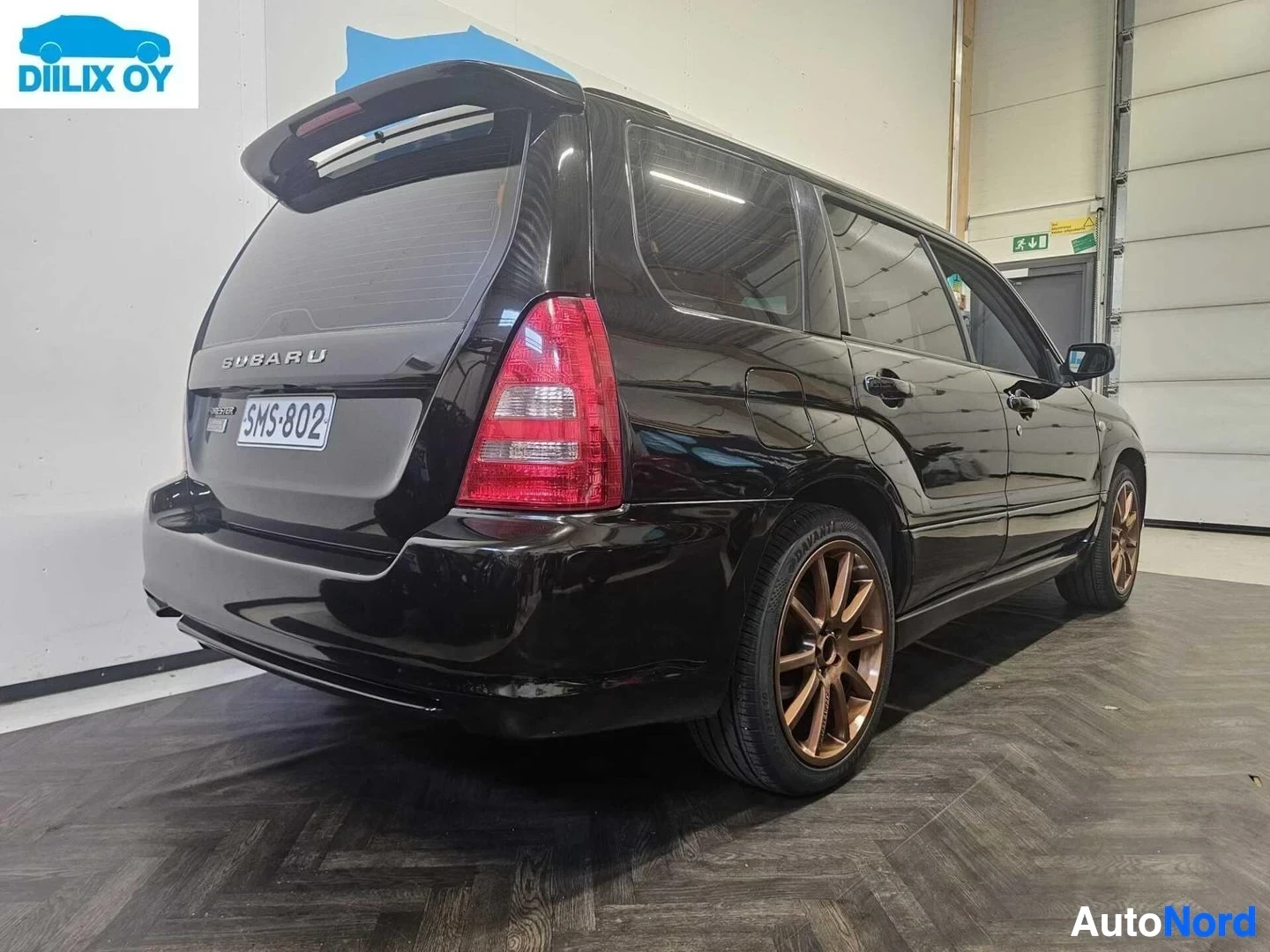Takaviisto: Musta Subaru maastoauto takaperästä ja oikealta, punaisella takavalolla ja pronssinkiharmailla vanteillaя. Teksti SUBARU takaikkunassa ja kilpi takavala