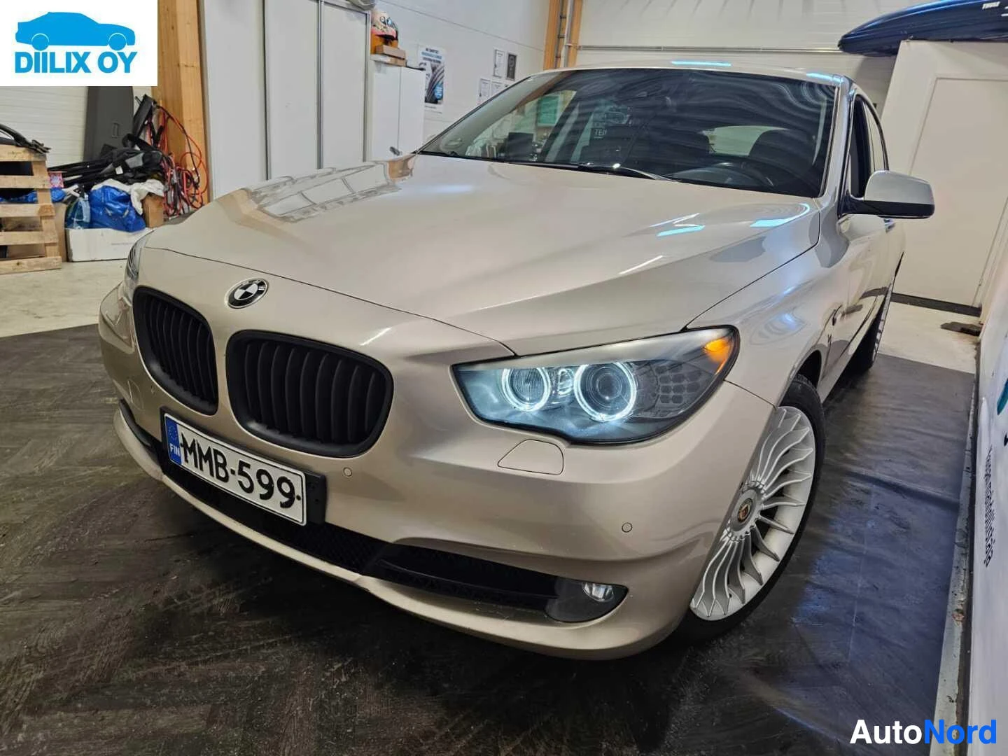 Etuviisto, nokka vasemmalle: Hopeanvärinen BMW Gran Turismo seisoo hallin lattialla, etunäkymä vasemmalle kääntyneenä. Auto on kylki näkyvissä, rengaspainikkeet näkyvät sivussa, re