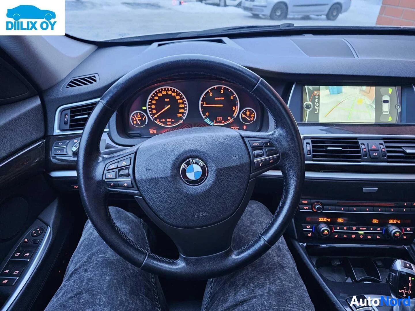 Ohjaamo: Auton kojelauta ja ratti, BMW-logo rattissa, digitaalinen näyttö kuljettajan edessä, ilmastoinnin säätöpainikkeet