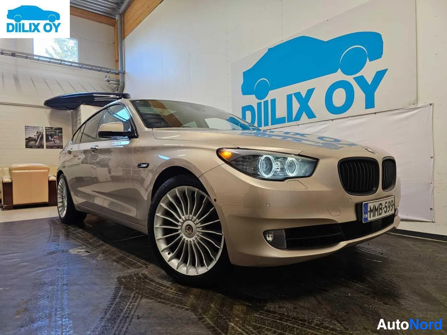 Etuviisto, nokka oikealle: Hopeanvärinen BMW Gran Turismo seisoo hallin lattialla sisänäkymässä, sivunäkymä oikealle kääntyneenä. Kulmikas etuosa ja kylki näkyvät. Rekisterikyltti