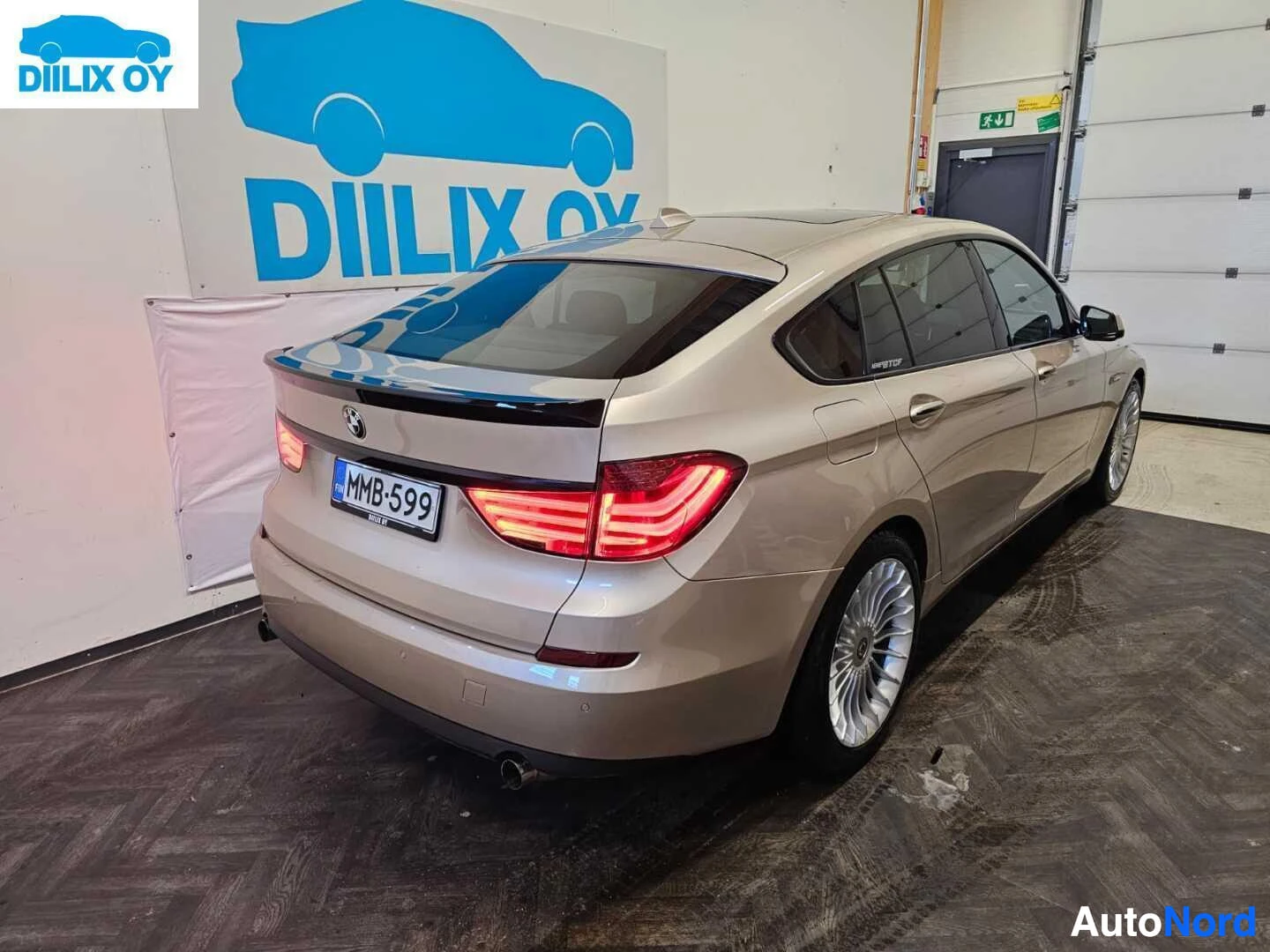 Takaviisto: Beige BMW Gran Turismon takaosa kolmen neljänneksen kulmasta, näkyy takavalot ja rekisterikylpi. Auto seisoo hallissa