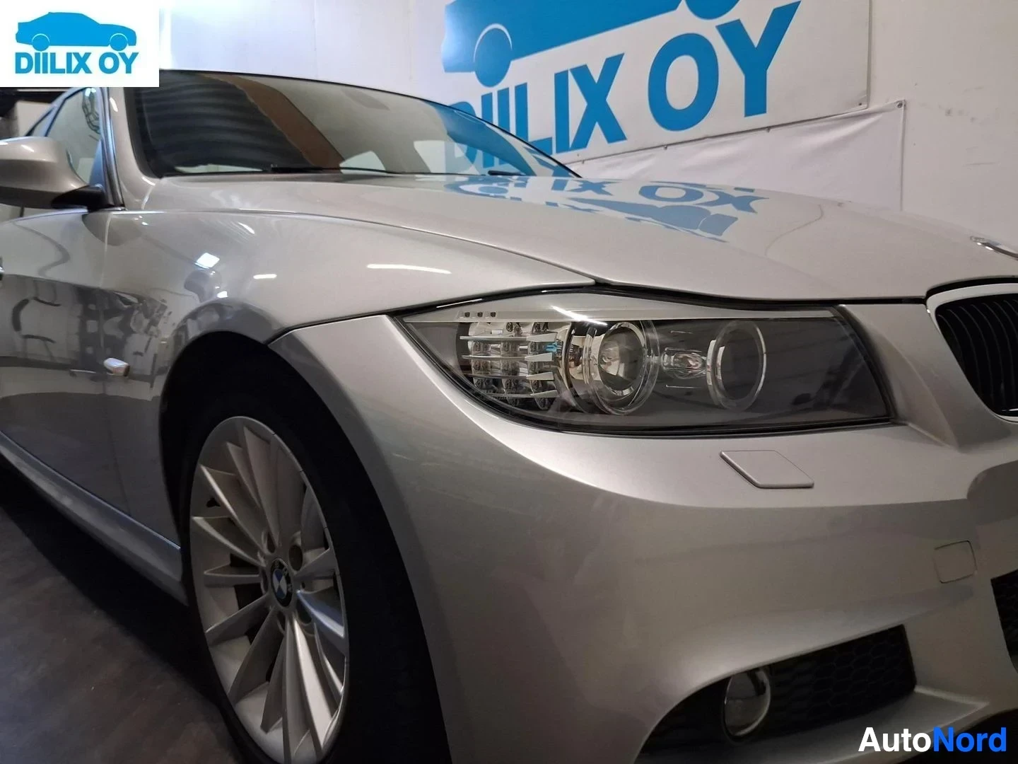Etuviisto, nokka vasemmalle: Hopea-värinen BMW sedan kuvattu vasemmalta keulasta, näkyvät etupuskuri, ajovalot ja alumiinivanteelliset renkaat.