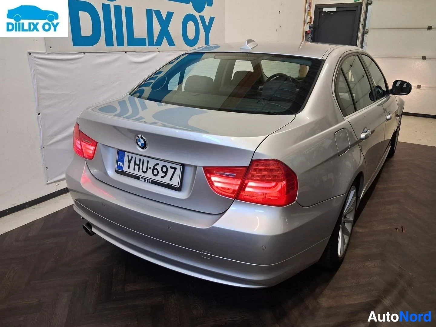 Takaa: Hopeanvärinen BMW-sedan takaosasta nähtynä. Rekisterikylpi näkyvä. Punaiset takavalot ovat päällä