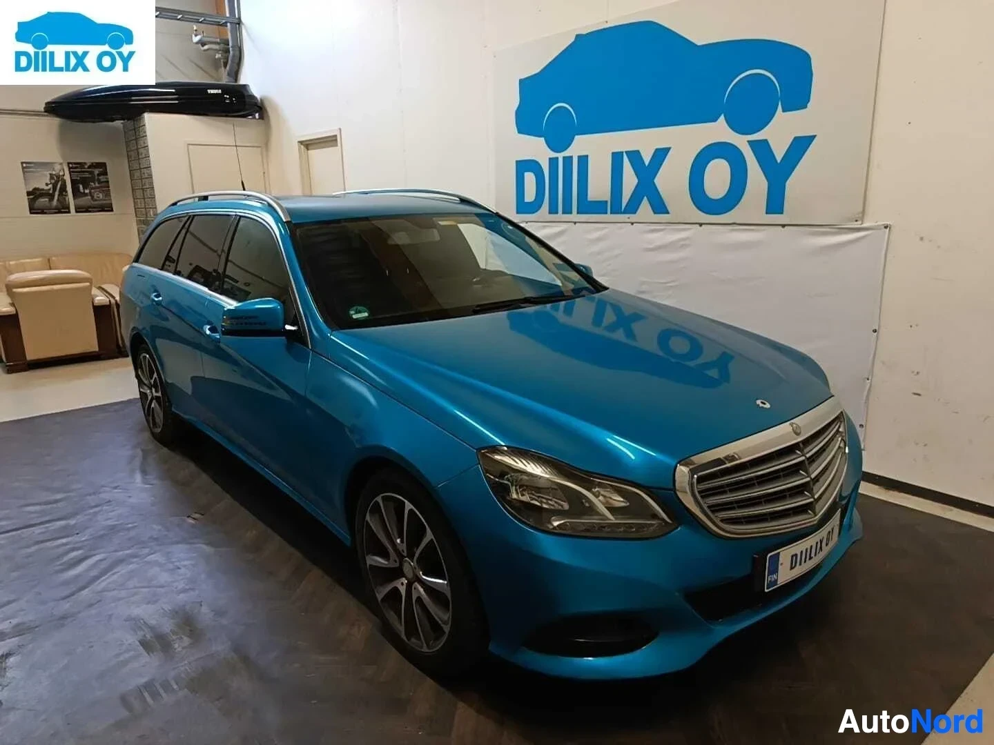 Etuviisto, nokka oikealle: Sininen Mercedes-Benz E-sarjan farkkuauto showroomissa, oikealle kääntynyt kulmasta kuvattuna.