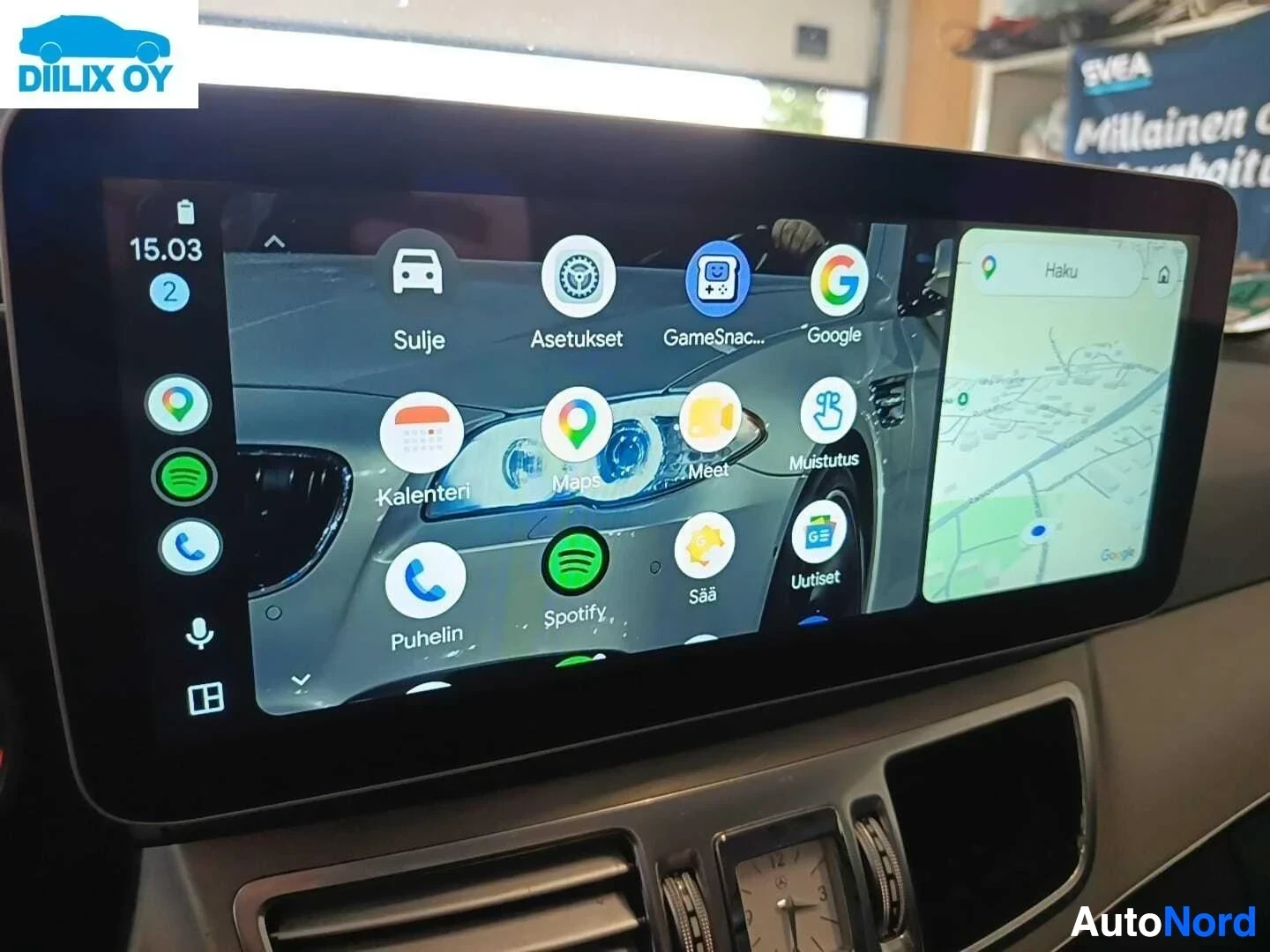 Yksityiskohta: Auton infotainment-näyttö näyttää sovelluksia ja navigaatiokarttaa.