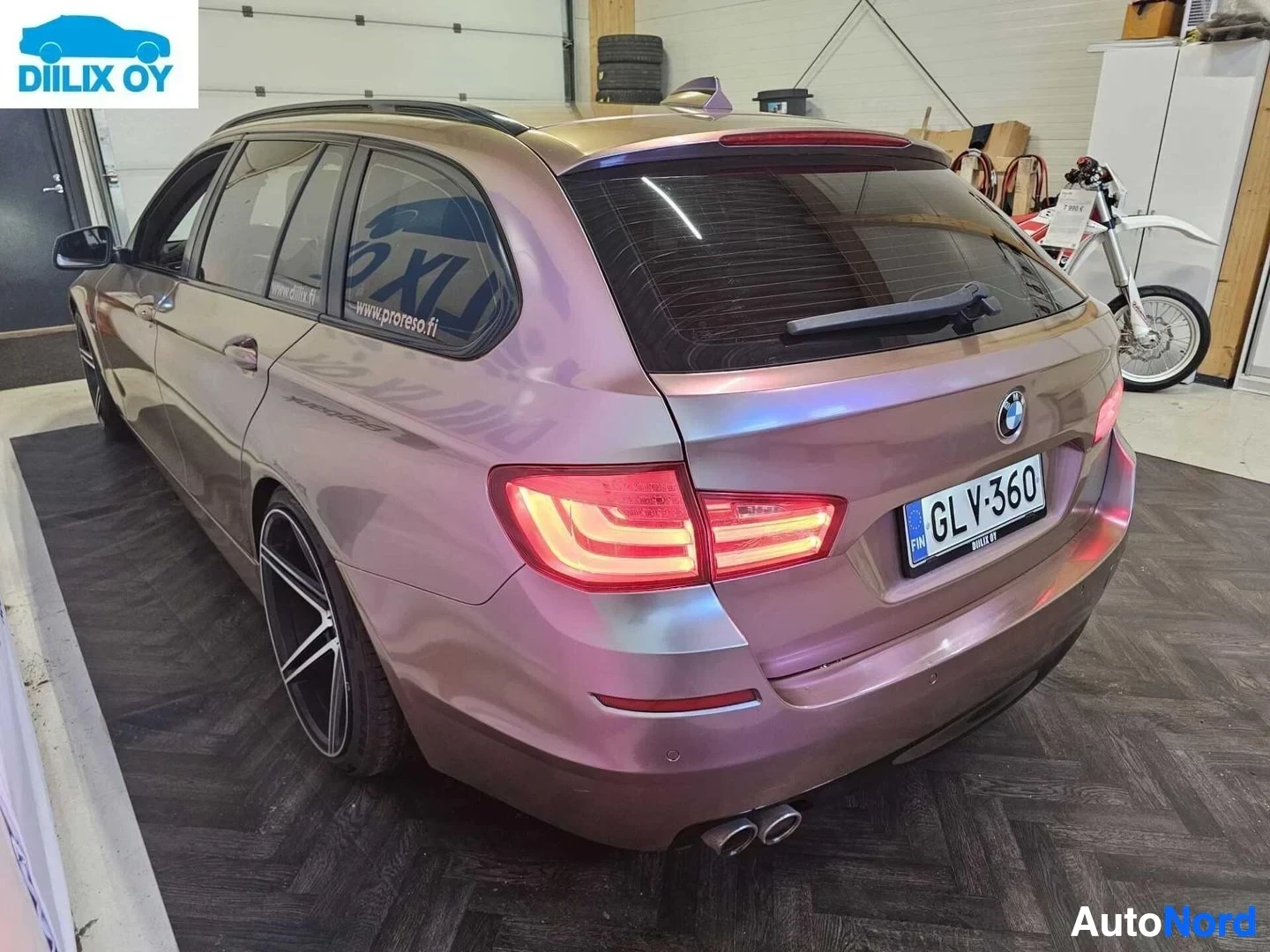 Takaviisto: Violetti BMW farmari, takanurkka oikealta, sisätiloissa. Rekisterikilpi näkyy. Punaiset takavallot palavat. Dual exhaust putket näkyvät takavasemmalla