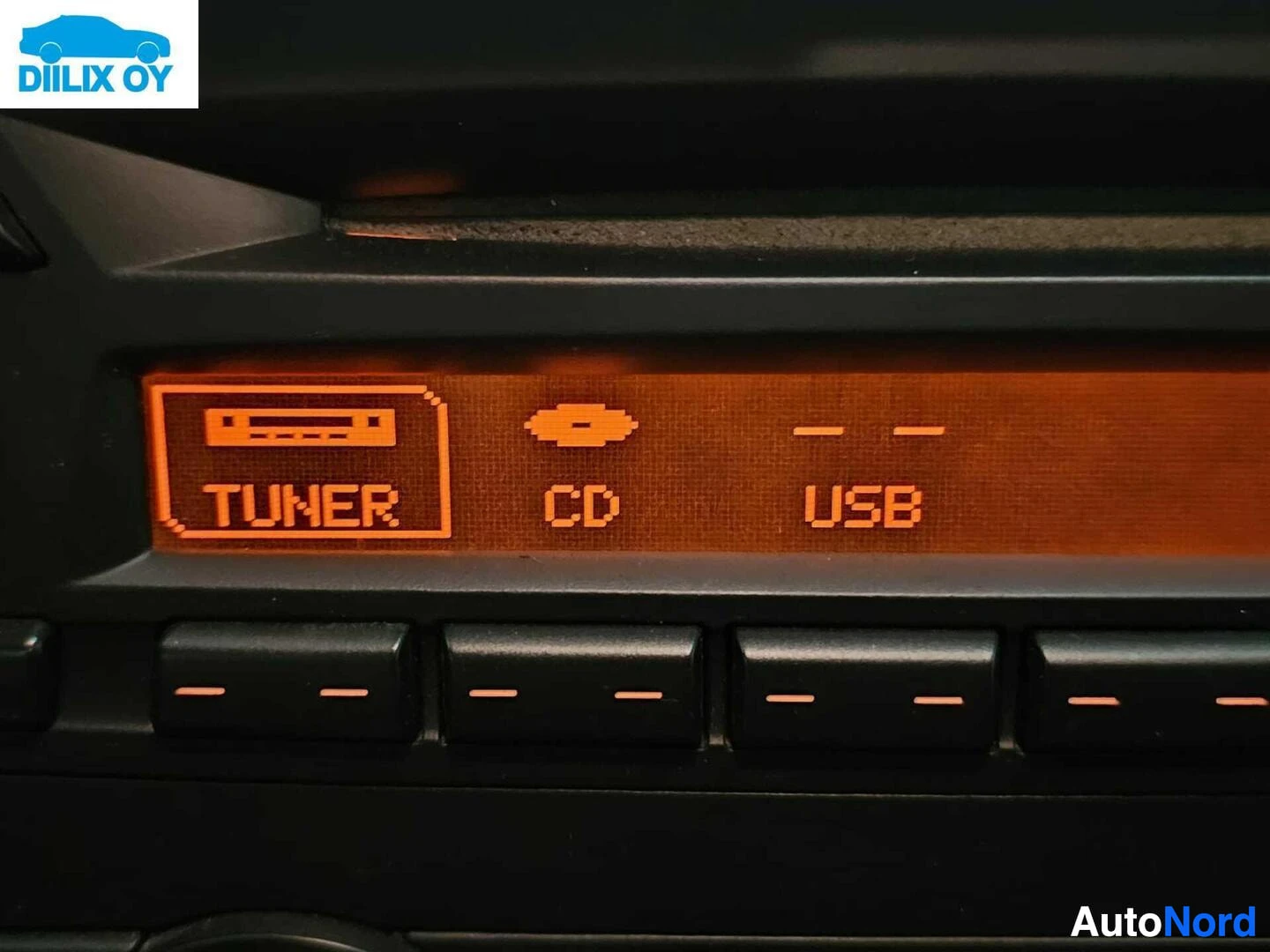 Yksityiskohta: Autoradion näyttöpaneeli, jossa näkyvät TUNER, CD ja USB -pikakset oranssilla tekstillä tummanharmaalla pohjalla, sekä alla multipainikkeet.