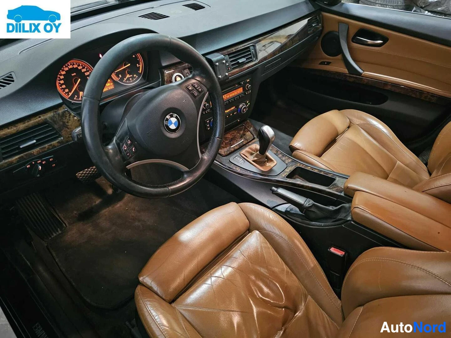 Ohjaamo: Auton sisusta, näkyvissä ruskeat nahkaistuimet, musta ohjauspyörä BMW-logolla, puu-efektin vähennykset, vaihteisto ja valaistu mittaristopaneeli oransseilla neu