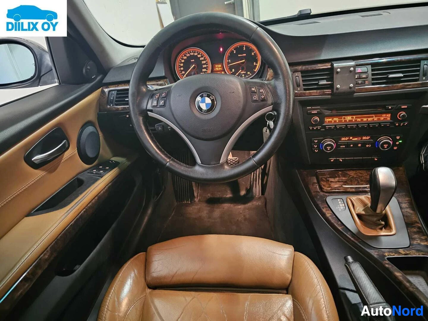 Ohjaamo: Auton ohjaamo etulta: ratti BMW-logolla, kombinaation kojelautanäytöt, ruskea ja musta sisustus, ohjainpyörän nappuloita ja keskikonsolissa nauhoitinta.