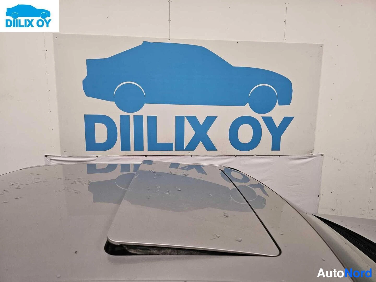 Muu: Valkoinen Mercedes-Benz sedan kuvan oikeassa reunassa näkyvissä, kojelaudan yläosan näkymä. DIILIX OY -logon heijastus auton kojelaudalla näkyvä. Varaston valko