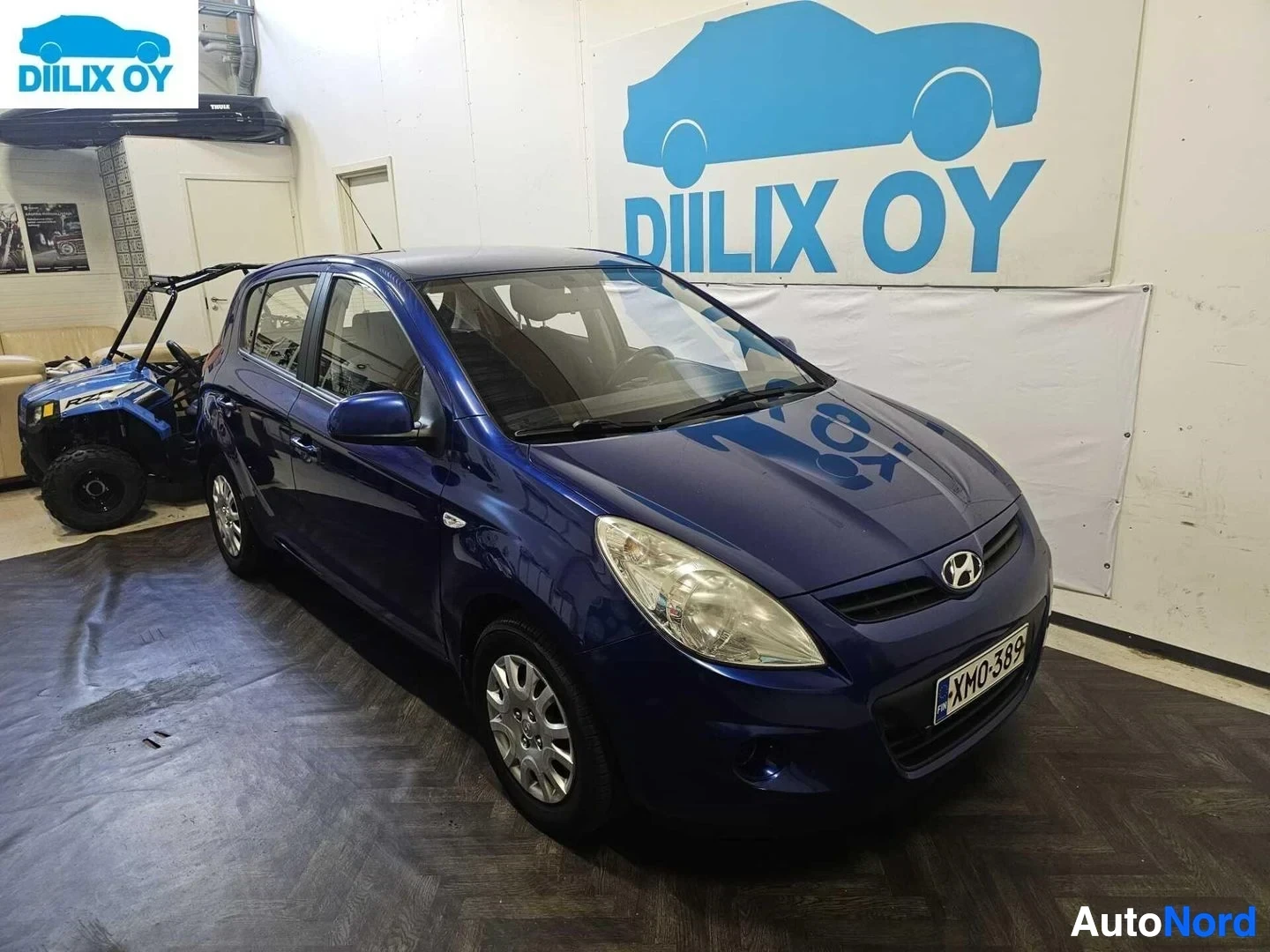 Etuviisto, nokka oikealle: Sininen Hyundai i20 -henkilöauto vasen etukulma, sisätiloissa