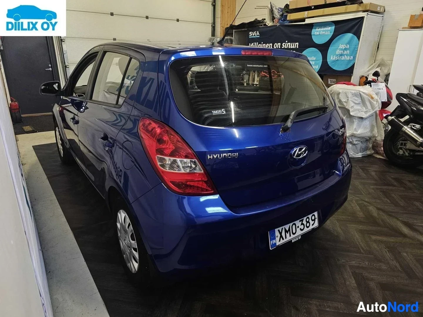 Takaa: Sininen Hyundai i20 -henkilöauto takaa, sisätiloissa, ovi auki