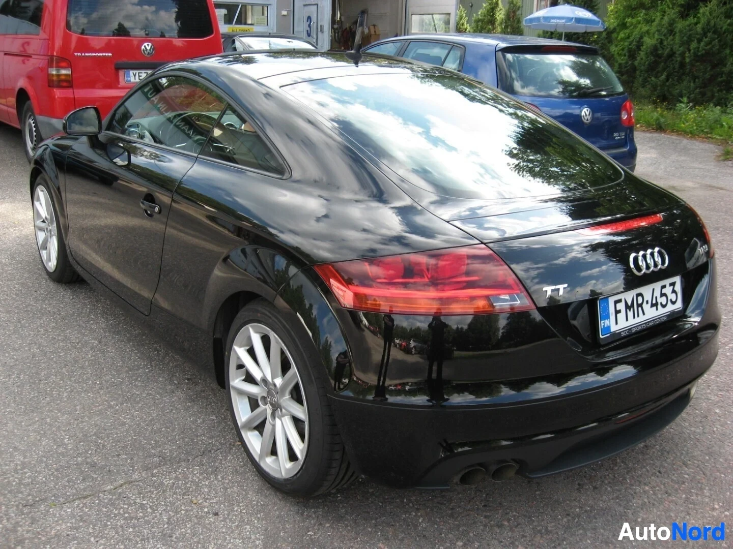 Takaviisto: Musta Audi TT -coupe takaosasta sivusta kuvattuna, TT-merkintä ja punainen takavalo näkyvissä, rekisteritunnus