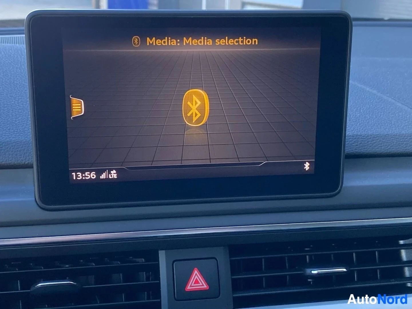 Yksityiskohta: Infotainment-näyttö näyttää 'Media: Media selection' -valikon Bluetooth-kuvakkeella ja radio-kuvakkeella, aika 13:56.