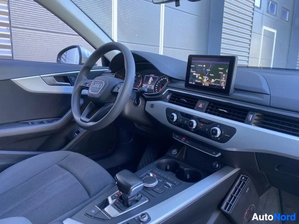 Etuistuimet: Audi-ohjauksinen ohjaustyöntö, instrumenttipaneeli navigointinäytöllä ja manuaalinen vaihteisto; ilmastointi-painikkeet näkyvät.