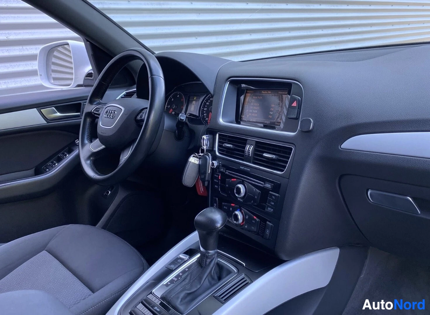 Ohjaamo: Audi Q5:n kuljettajan puoleinen sisustanäkymä, näkyy Audi-ohjauspyörä, digitaalinen välikilpi, kosketusnäyttö, ilmastointi-ohjaimet ja manuaalinen vaihteisto.
