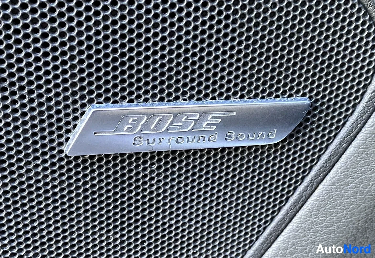 Yksityiskohta: Bose Surround Sound kaiuttimen tunniste metalliverkkoisen sisäkaton paneelissa.