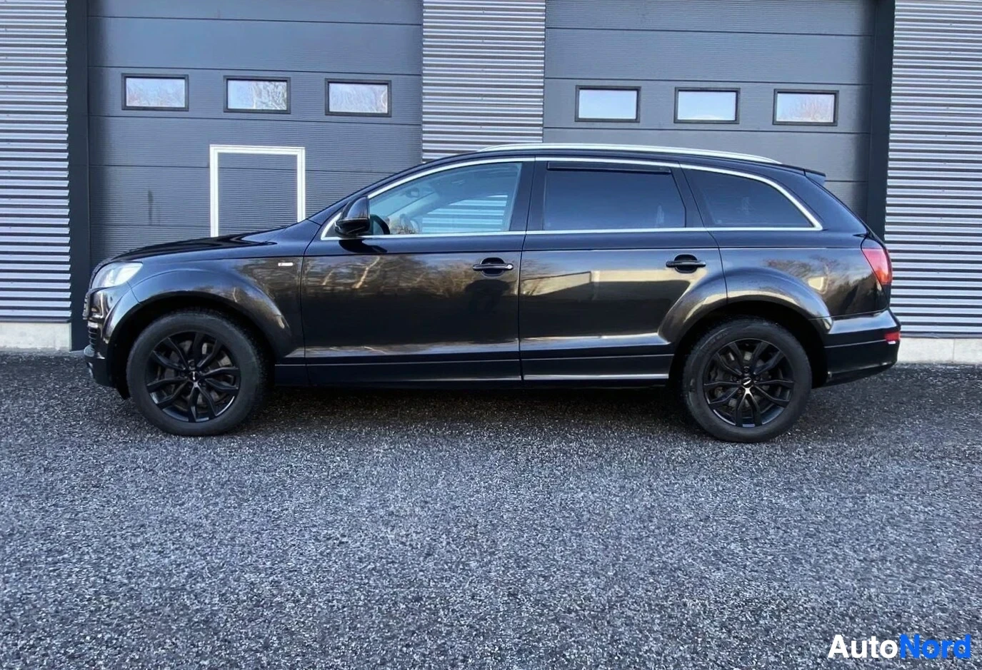 Sivulta: Musta Audi Q7 sivusta kuvattuna, kokonaisnäkymä ajoneuvon oikeasta sivusta varikko-ovin edessä
