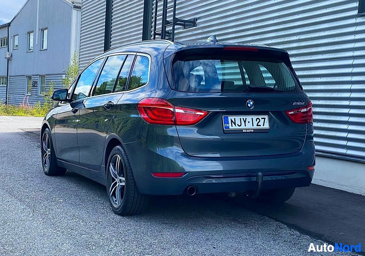 Takaviisto: Sinisen BMW-tila-auton takapuoli ja sivu näkyvissä, punaisia takavaloja ja rekisterikilpeä NJY·127 näyttäen. Merkintä '218d' näkyy takalisäkkeessä.