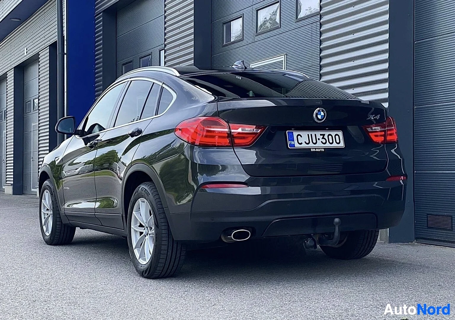 Takaviisto: Musta BMW X4 takaa ja sivusta katsottuna, rekisterinumero näkyvissä, punaiset takavalaistaimet, metalliset vanteet, tokaisu näkyvissä, teollisuusrakennu