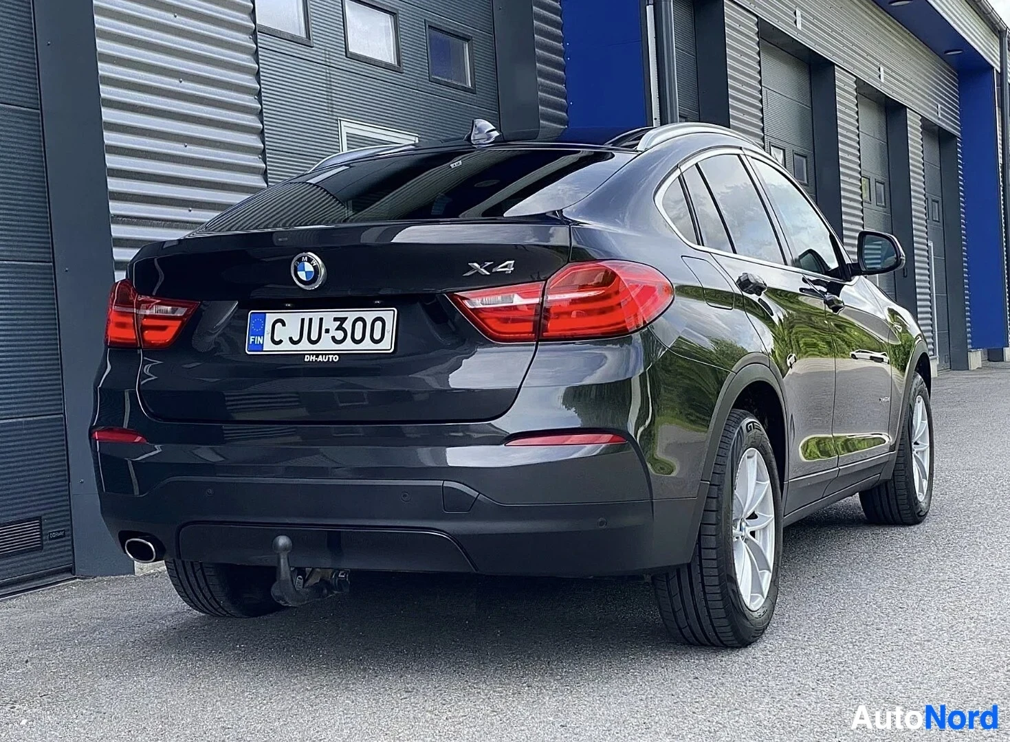 Takaa: Musta BMW X4 takaa katsottuna, rekisterinumero, punaiset takavalaistaimet, metalliset vanteet, tokaisu näkyvissä, teollisuusrakennuksen harmaa seinä tau
