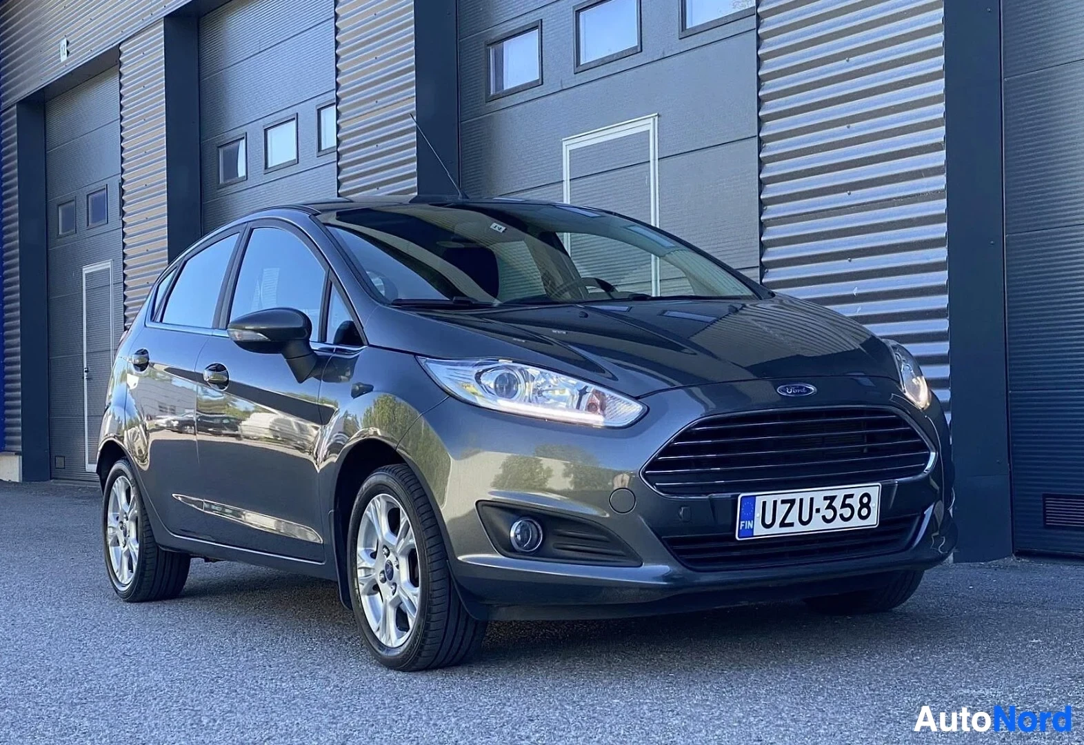 Sivulta: Tummansininen Ford Fiesta sivuprofiilista vasemmalta, rekisterikilvessä, teollisuushallien edessä