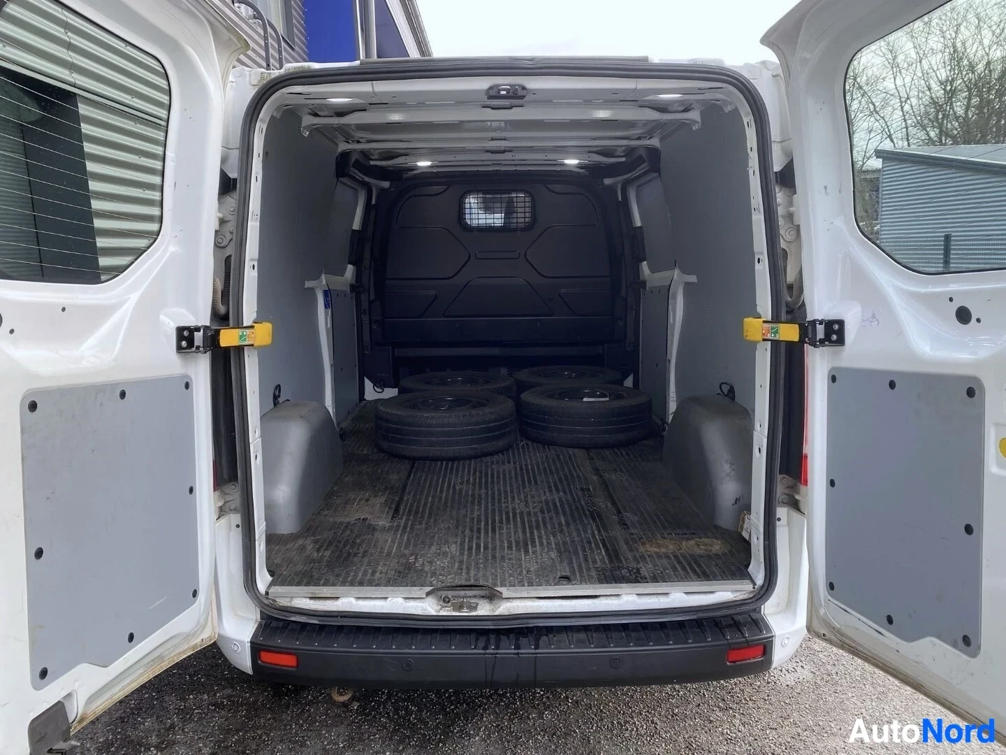 Tavaratila: Valkoinen pakettiauto, takaoven avoin, näkyy kuormatilavuo sisällä renkaineen.