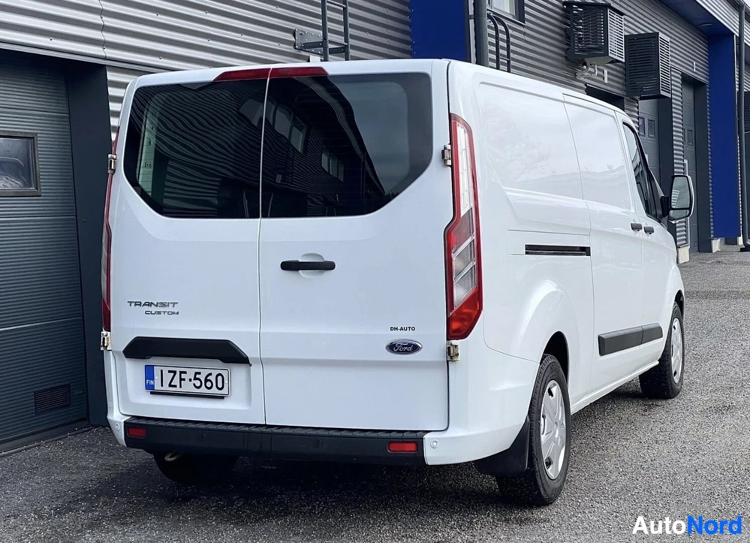 Takaviisto: Valkoinen Ford Transit Custom -pakettiauto kuvattu takaa oikealla puolella, rekisterikilvessä, takaosassa näkyy TRANSIT CUSTOM ja DH AUTO -teksti