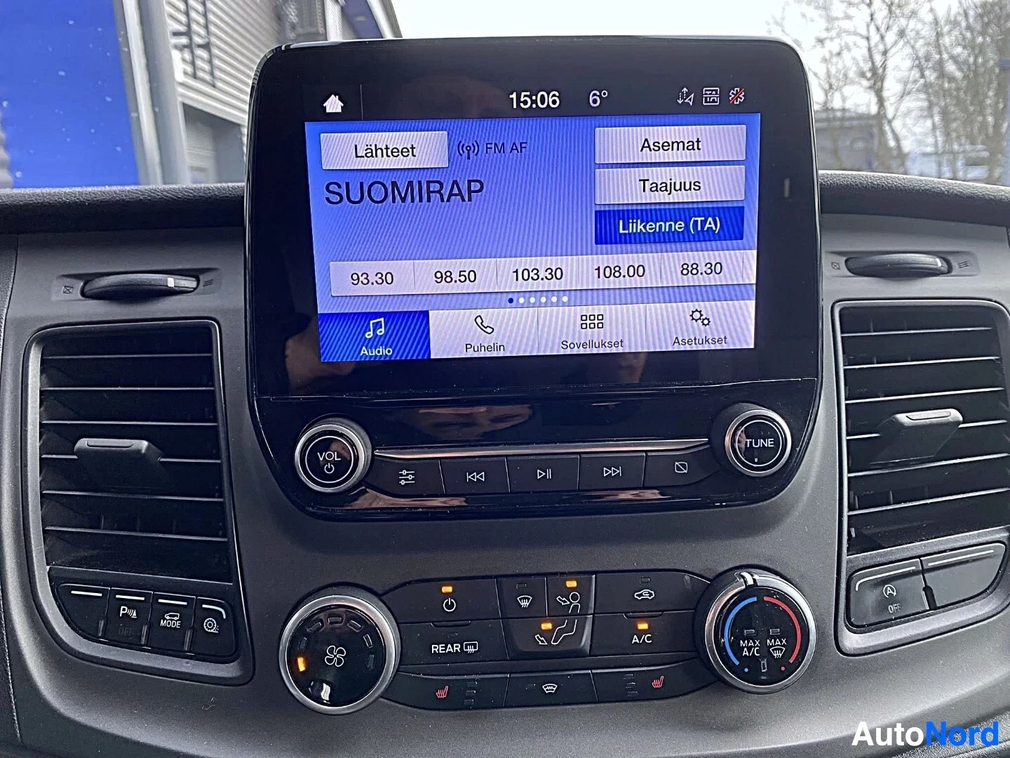 Ohjaamo: Ajoneuvon sisäkuva keskikonsolin näytöltä, joka näyttää radio-sovelluksella olevan suomalaisia radiokanavia (Lähteet, FM AF, Asemat, Taajuus, Liikenne TA) ja ke
