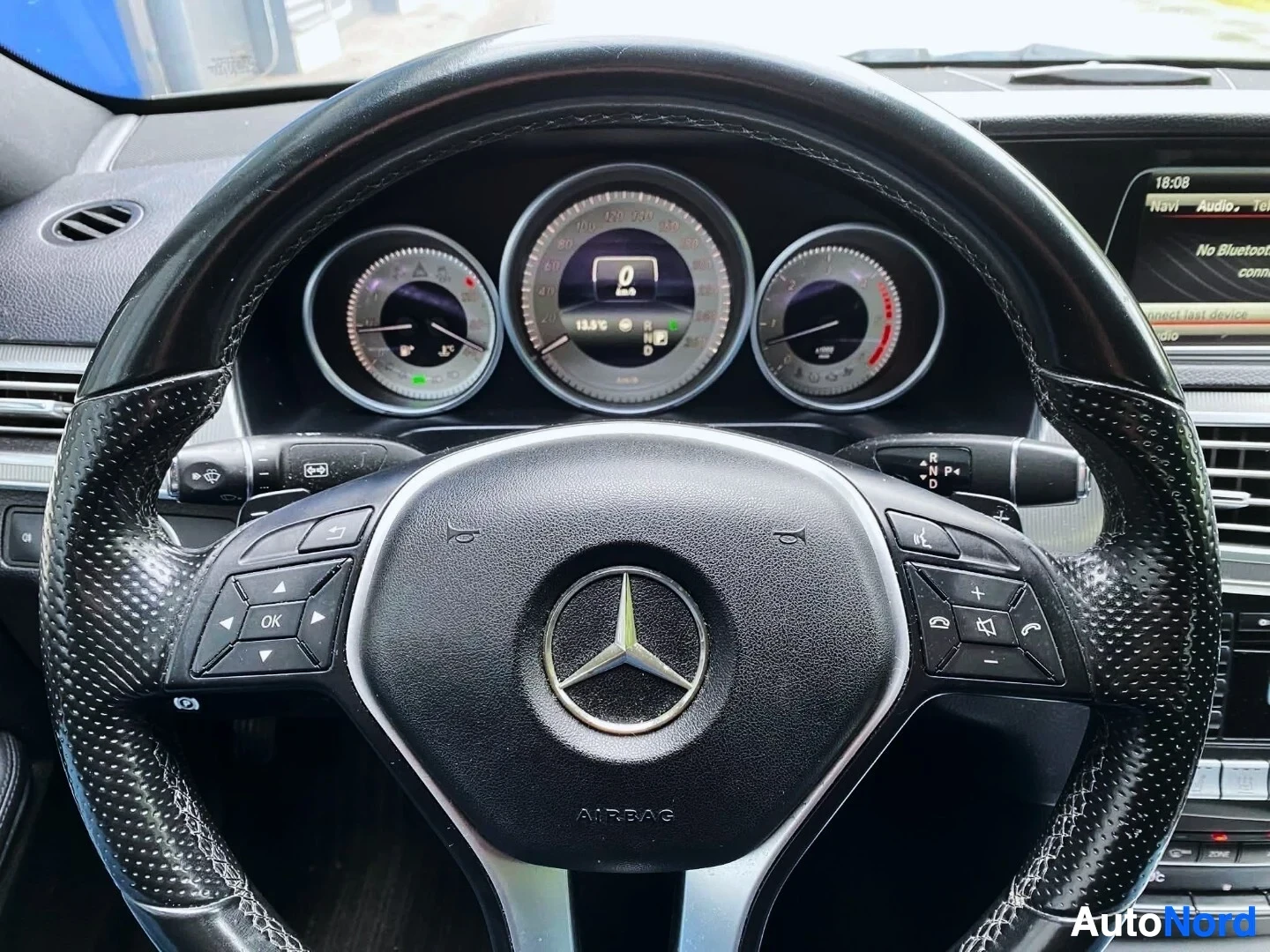 Yksityiskohta: Ohjauspyörä Mercedes-Benz logolla, musta nahkainen, monikäyttöinen ohjainpainikkeet molemmin puolin. Mittaristo näkyy taustalla.