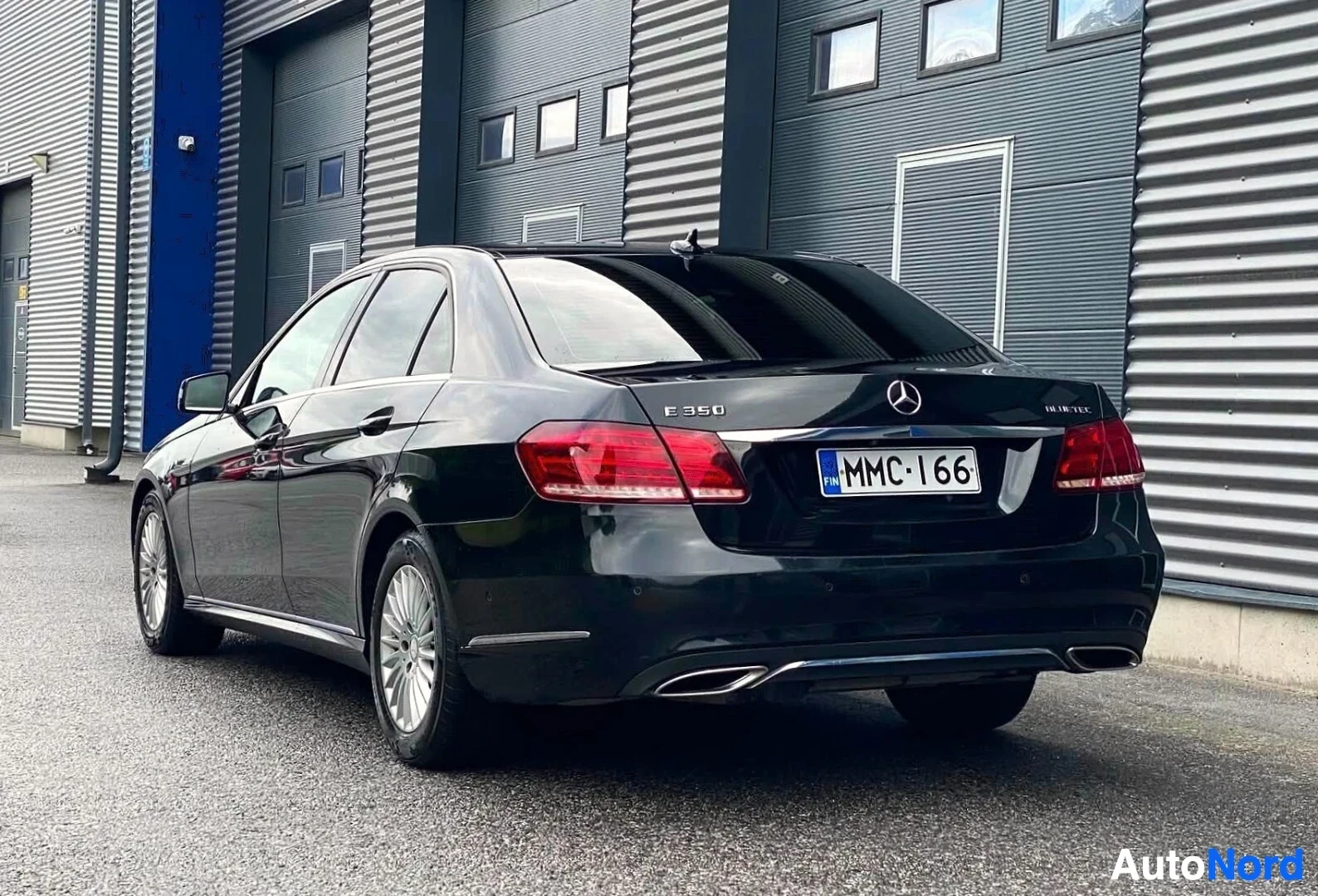 Takaviisto: Musta Mercedes-Benz E-sarjan sedan takavasemmalta puolelta, rekisterikilpi MMC·I66, takaluukulla E350 ja BlueTec -merkinnät